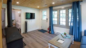 A cozy room with a fireplace, a television mounted on the wall, a dining table with a tray, and a window with curtains. - Hydrus cozy 2 bedroom cottage (Kawartha Lakes)