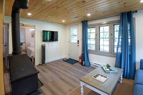 Una habitación acogedora con chimenea, televisor montado en la pared, mesa de comedor con bandeja y ventana con cortinas.