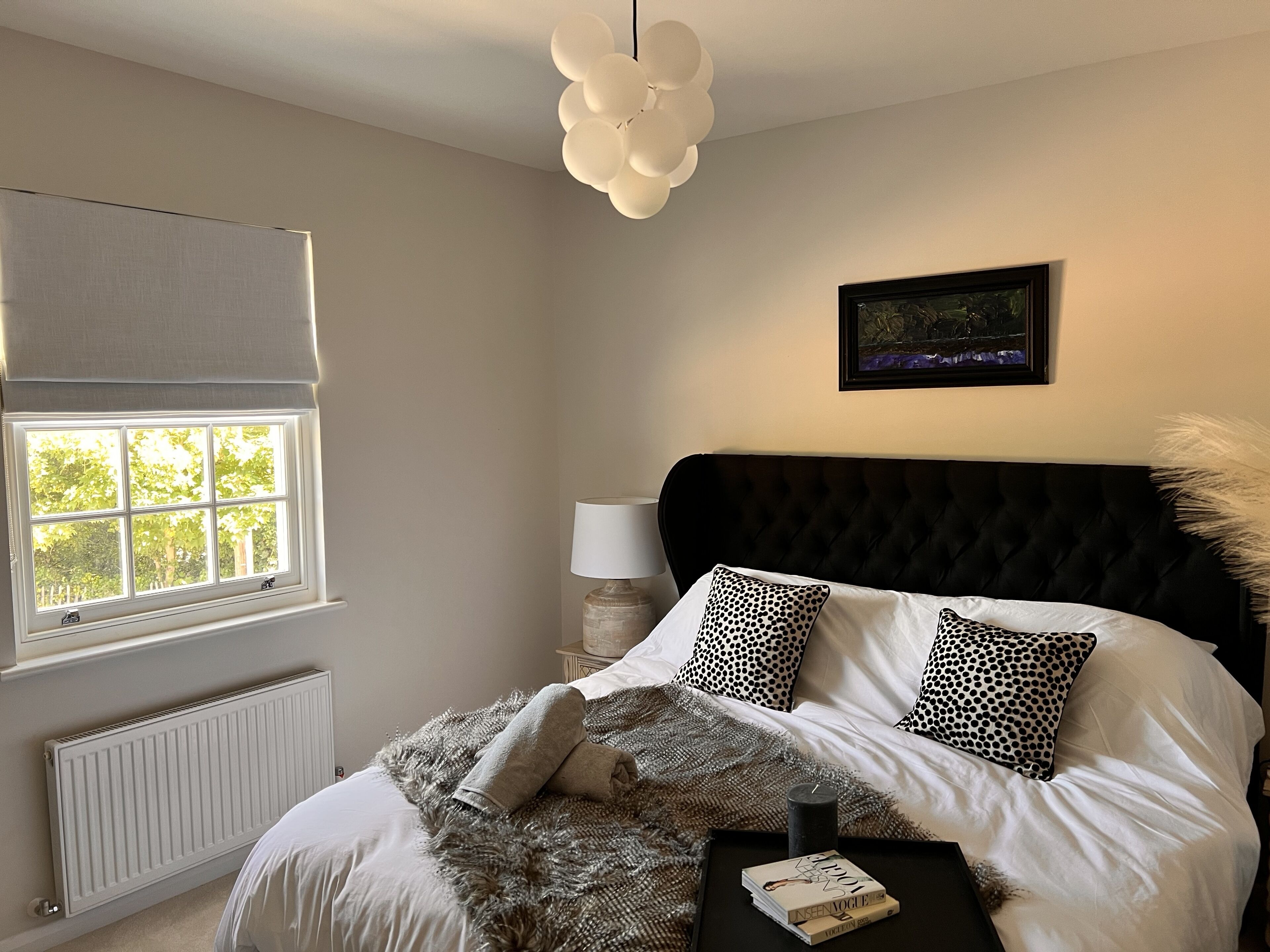 A bedroom with a large window, a black tufted headboard, and a framed picture on the wall.
