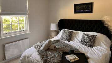 A bedroom with a large window, a black tufted headboard, and a framed picture on the wall.