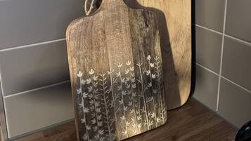 A wooden cutting board with a handle and a decorative pattern, placed on a tiled floor next to a wall.