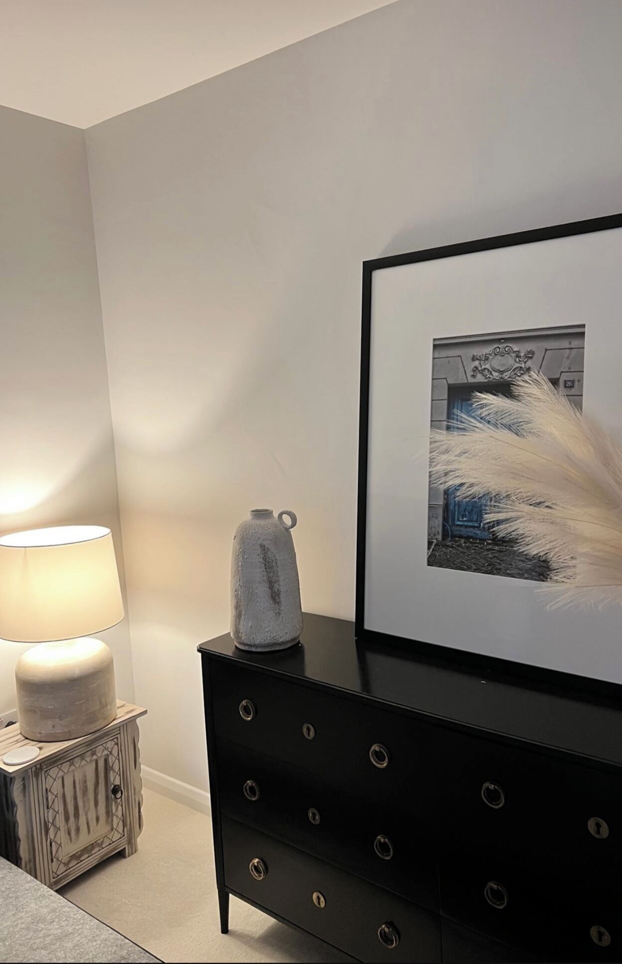 A modern room with a black dresser, a framed picture on the wall, a lamp, and a decorative vase.