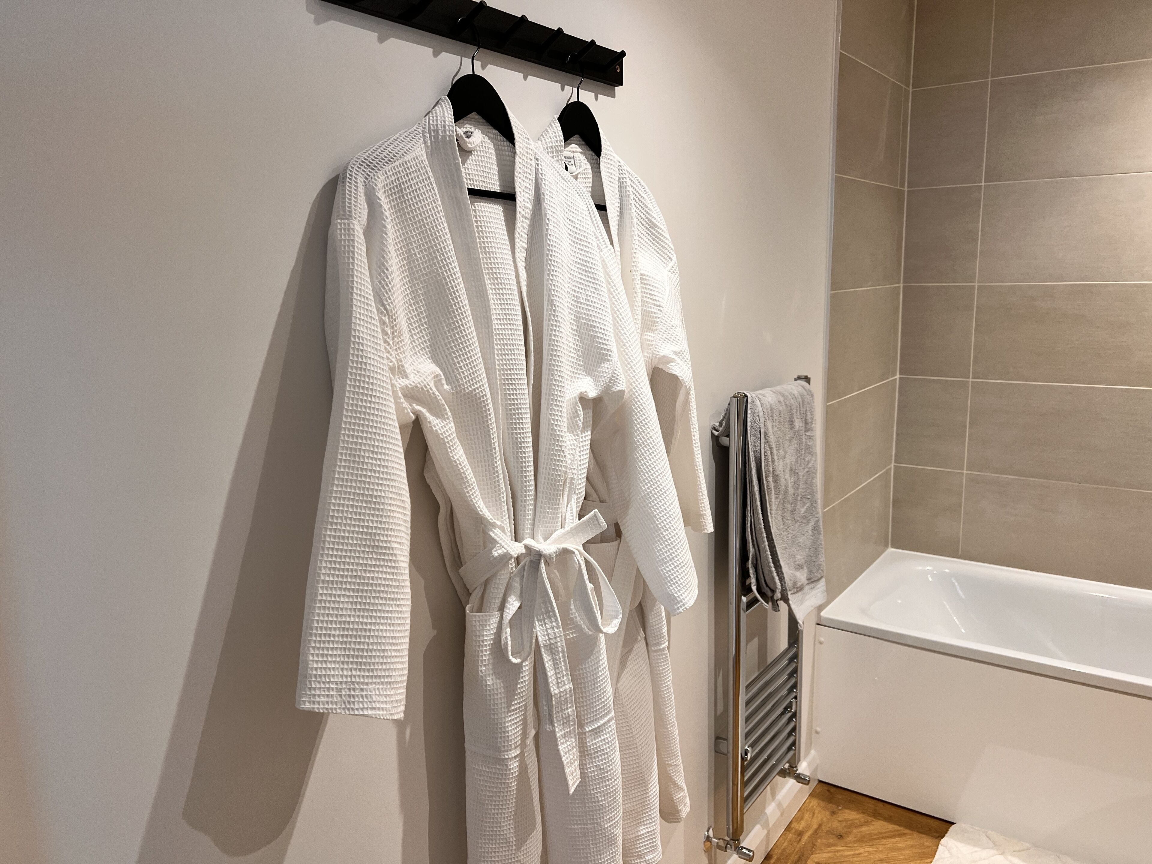 Un bagno con una vasca, un portascopevoli con due accappatoi bianchi e un asciugamano appeso al muro.