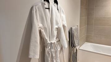 Un bagno con una vasca, un portascopevoli con due accappatoi bianchi e un asciugamano appeso al muro.