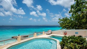 Piscina com vista clara para o oceano e uma espreguiçadeira.