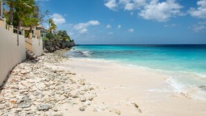 Uma praia com costa rochosa, água turquesa cristalina e céu claro.