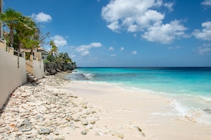 Ein Strand mit felsigem Ufer, klarem türkisblauem Wasser und blauem Himmel.