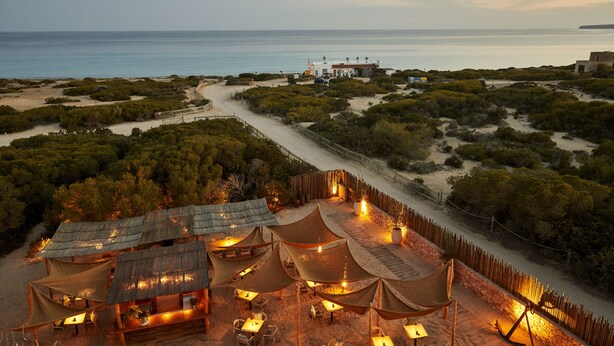 A beachfront resort with thatched-roof huts, outdoor seating, and a view of the sea. - Hotel Teranka (Formentera)