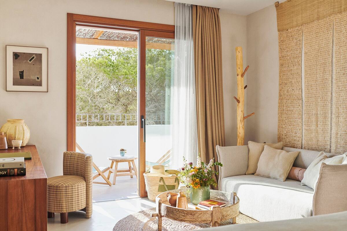 A room with a sofa, a chair, a coffee table with books and a vase, a wooden side table, and a framed picture on the wall.