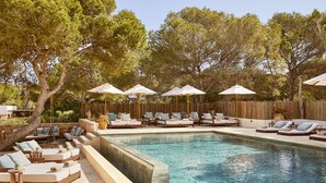 A poolside area with lounge chairs, umbrellas, and a wooden fence. - Hotel Teranka (Formentera)