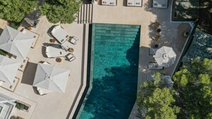 An aerial view of a swimming pool surrounded by lounge chairs and umbrellas, with trees in the background. - Hotel Teranka (Formentera)