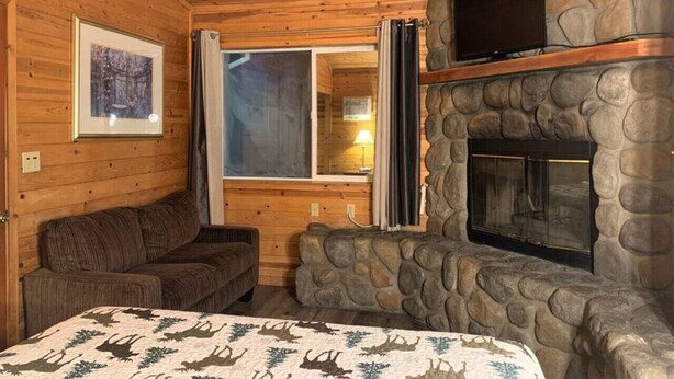 Une chambre confortable dans un chalet, avec une cheminée en pierre, des murs en bois, un canapé et un lit recouvert d’une couverture à motifs.