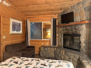 Cozy cabin-style room with a stone fireplace, comfortable couch, and a bed with a patterned bedspread.
