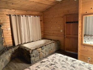 Una cabaña de madera con una bañera de piedra, una puerta de madera y una ventana con cortinas.