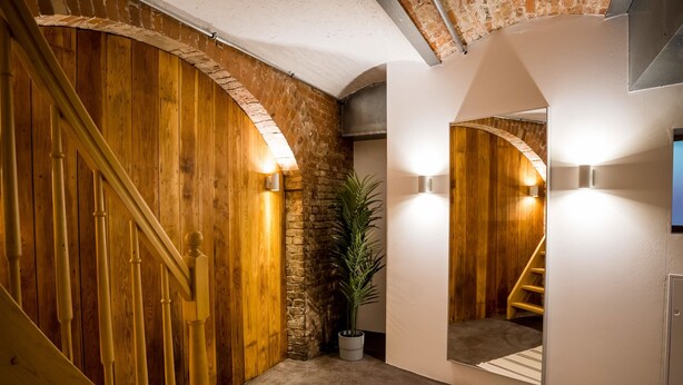 A wooden staircase with a handrail, a potted plant, and a wall-mounted mirror reflecting a staircase. - Großzügige Wohnung in Berlin Mitte für 6 Gäste (Berlin)