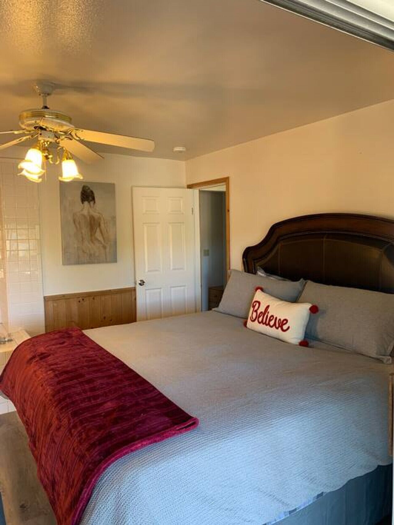 A bedroom with a large bed, a ceiling fan, a door, and a wall-mounted painting.