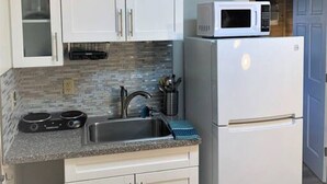 Una cocina compacta con gabinetes blancos, un lavamanos de acero inoxidable, un microondas y un horno empotrado.
