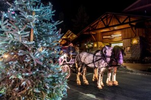 Un sapin de Noël illuminé et une calèche tirée par des chevaux devant un bâtiment portant l’inscription « Village Inn ».