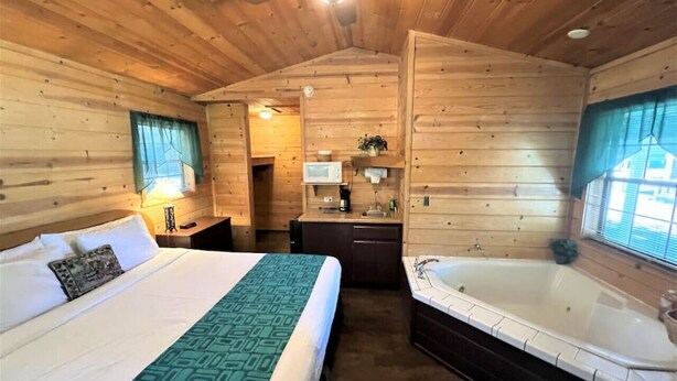 A cabin-style room with a large bed, a separate bathroom with a bathtub, and a kitchenette area. - Unique 1 BDRM with Jetted Hot Tub - Bear Manor #5 (Big Bear Lake)