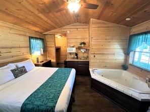 Une chambre de style cabane avec un grand lit, une salle de bain séparée avec une baignoire et un coin cuisine.