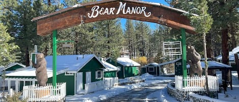 A wooden archway with "Bear Manor" written on it, leading to a row of green cabins with white railings.
