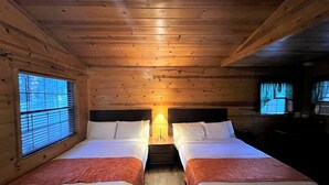 Una cabana amb dos llits, parets de fusta i una finestra amb persianes.