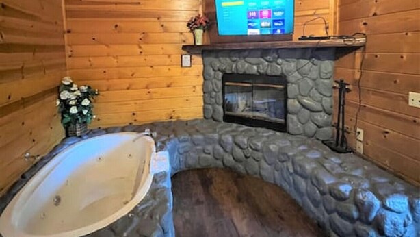 Interior d'una cabana de fusta amb una llar de pedra, una banyera d'hidromassatge de pedra i una televisió penjada.