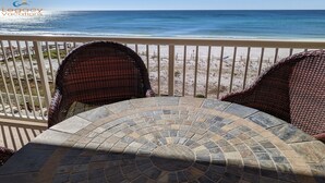A balcony with wicker chairs and a stone-tiled table overlooking a beach. - Azure 414 - 3 Bd Beachfront w/ Premium Amenities - Sleeps 8! (Fort Walton Beach)