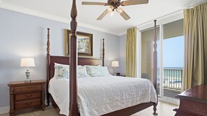 A four-poster bed with a ceiling fan, two bedside lamps, a nightstand, and a view of the beach through a sliding glass door. - Azure 414 - 3 Bd Beachfront w/ Premium Amenities - Sleeps 8! (Fort Walton Beach)
