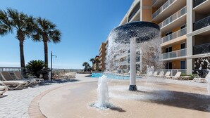 A water fountain surrounded by lounge chairs and a pool, with a multi-story building in the background. - Azure 414 - 3 Bd Beachfront w/ Premium Amenities - Sleeps 8! (Fort Walton Beach)