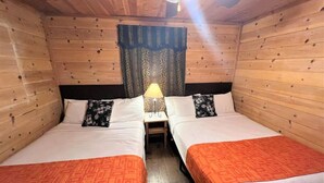 A cabin-style room with two beds, wooden walls, a ceiling fan, and a nightstand with a lamp. - BM #9 · Peaceful, Unique Hot Tub in Kitchen - Bear Manor#9 (Big Bear Lake)
