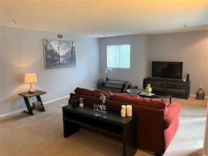 A living room with a red sofa, a coffee table, a TV, and a picture frame on the wall.