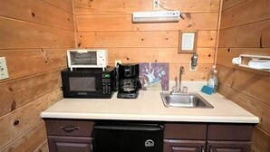 A compact kitchen with wooden walls, a microwave, a coffee maker, a sink, and a dishwasher.