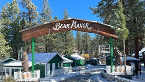 A wooden archway with "Bear Manor" written on it, leading to a row of green cabins with white railings.