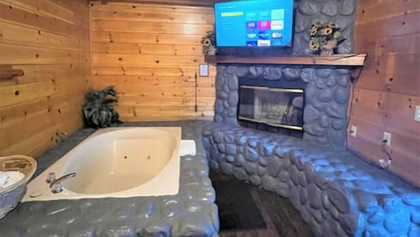 A wooden cabin interior with a stone wall, a large bathtub, and a mounted television.