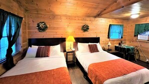 A wooden cabin room with two beds, a table, and a window with curtains.