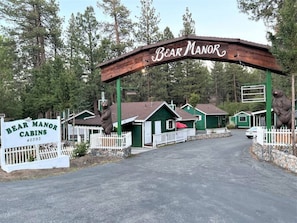 Bear Manor cabins with a wooden arch entrance, green cabins, and a white picket fence.