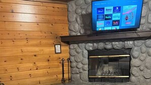 Une salle de bain avec un mur en pierre, un plancher en bois, une baignoire, un lavabo et un téléviseur à écran plat fixé au-dessus de la baignoire.