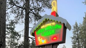 A sign for Crazy Hull Lodge with a neon welcome sign, a vacancy sign, and a Rustic Family Cabins sign.