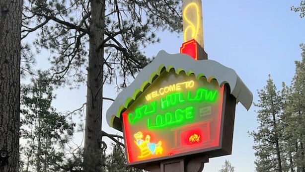 A sign for Crazy Hull Lodge with a neon welcome sign, a vacancy sign, and a Rustic Family Cabins sign. - Spacious, Fun Family Cabin - Cozy Hollow Lodge #2 (Big Bear Lake)