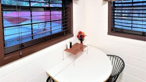 Una habitación con una mesa redonda y dos sillas, una ventana con persianas y una cortina.