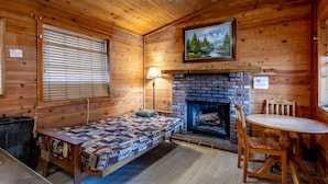 A cozy cabin room with a bed, a fireplace, a dining table, and a painting on the wall.