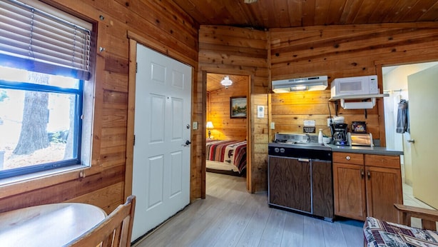 A cabin interior with a wooden interior, a kitchen area with a microwave, and a bed with a blanket.