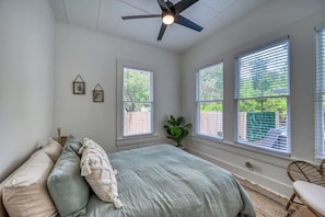 A bedroom with a bed, a ceiling fan, and three windows with blinds.