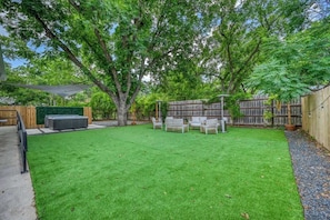 Un patio trasero con césped, mobiliario exterior, una valla de madera y árboles.