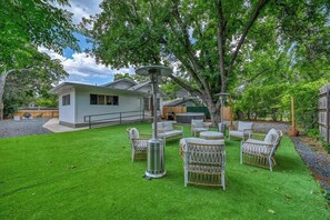 A house with a well-maintained lawn, outdoor furniture, and a large tree providing shade. - Luxury and Location With Hottub! (Fredericksburg)