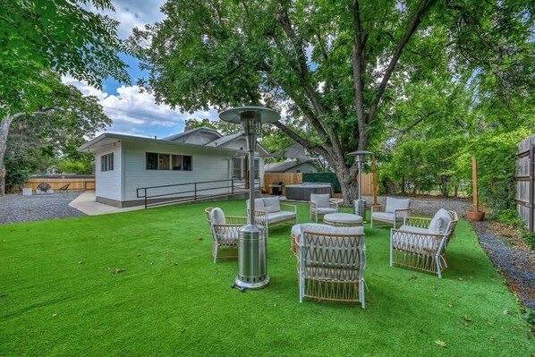 A house with a well-maintained lawn, outdoor furniture, and a large tree providing shade.