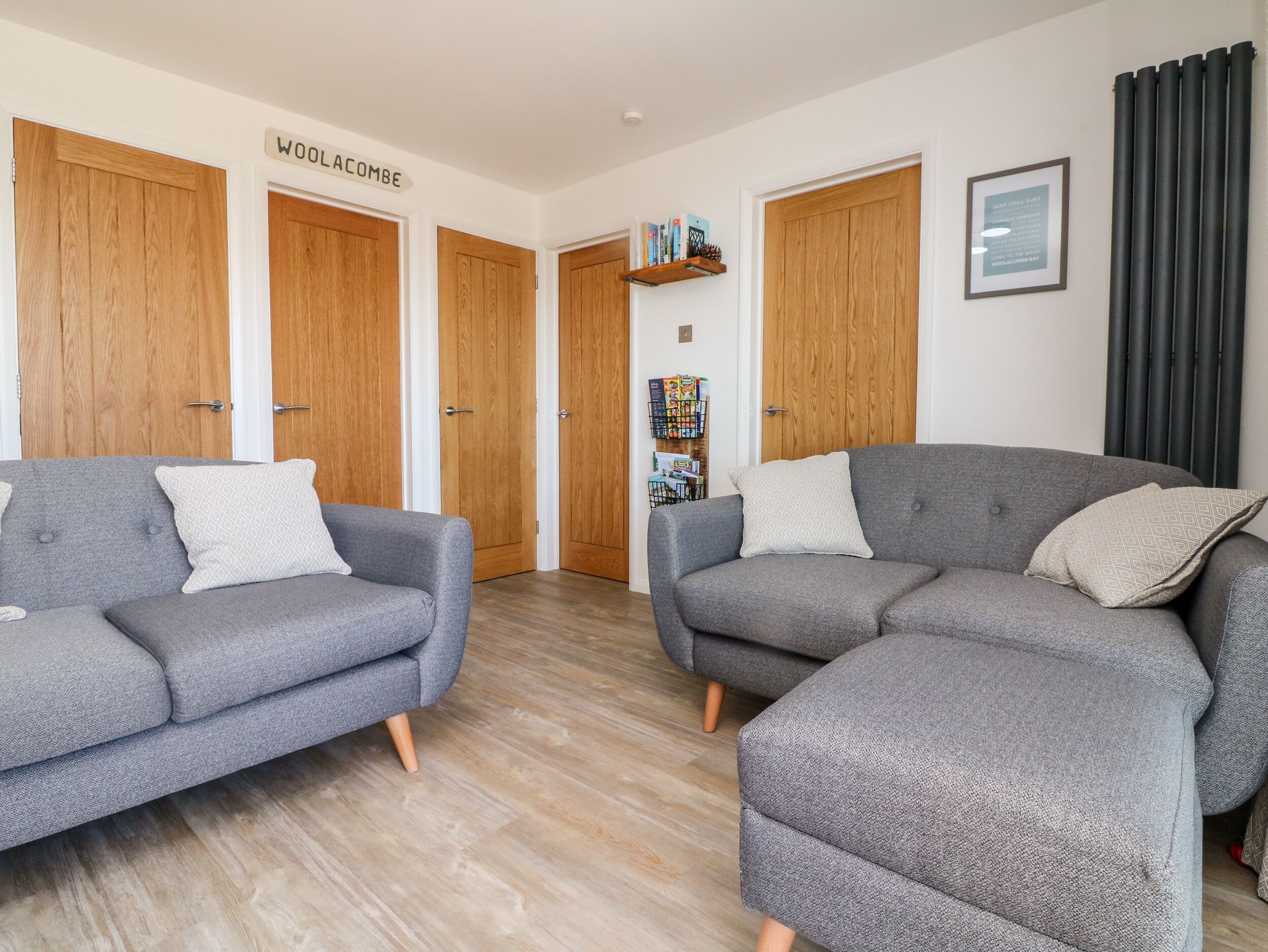 A modern living room with two grey sofas, wooden doors, a bookshelf, and a framed sign.