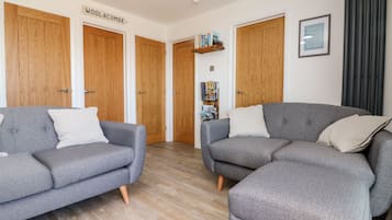 A modern living room with two grey sofas, wooden doors, a bookshelf, and a framed sign.