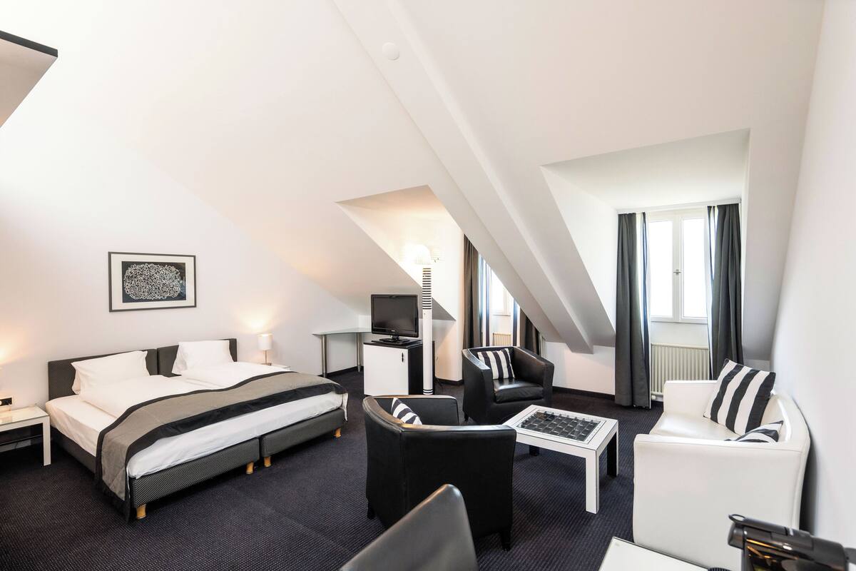 A modern hotel room with a bed, two armchairs, a coffee table, a desk, and a TV.